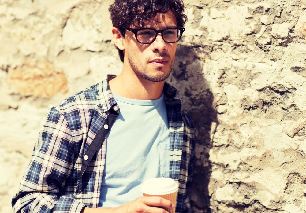 lifestyle, drinks and people concept - man in eyeglasses drinking coffee from disposable paper cup over street wall. man in eyeglasses drinking coffee over street wall