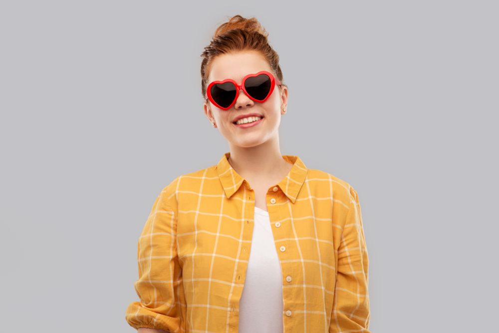 summer, valentine&rsquo;s day and people concept - smiling red haired teenage girl in checkered shirt and heart-shaped sunglasses over grey background. red haired teenage girl in heart-shaped sunglasses