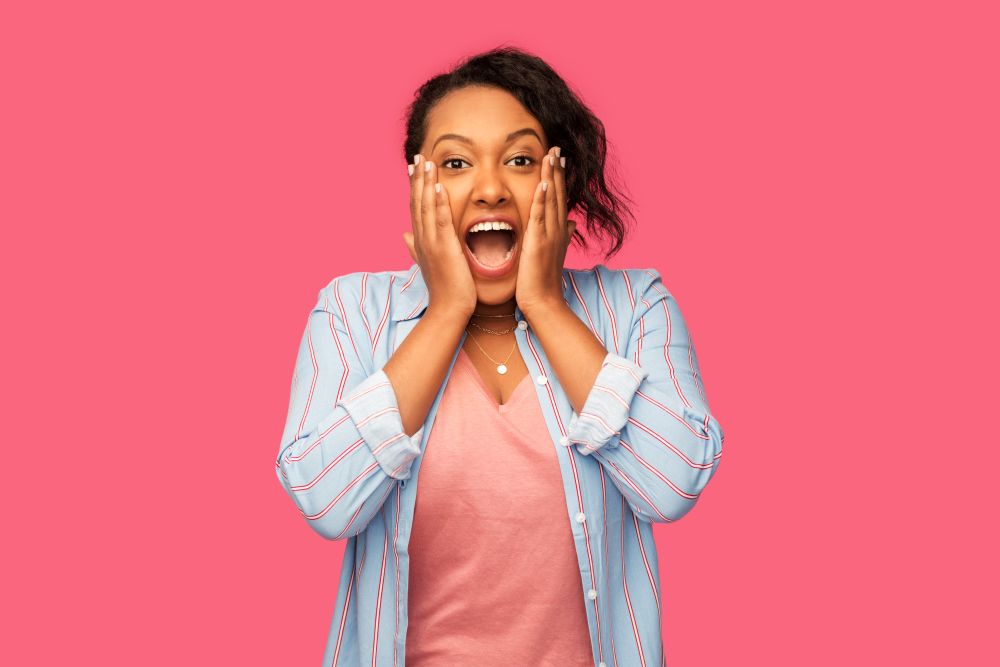 people, expression and emotion concept - happy amazed african american young woman over pink background. happy african american woman over pink background
