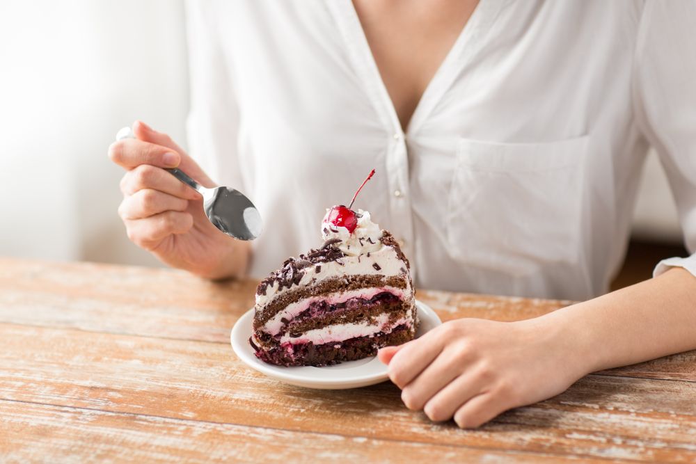 food, dessert and pastry concept - close up of woman eating piece of chocolate layer cake with maraschino cherry. woman eating piece of layer cake with cherry