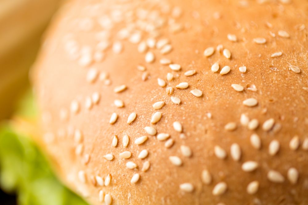 fast food and unhealthy eating concept - close up of hamburger bun crust with sesame seeds. close up of hamburger bun crust with sesame seeds