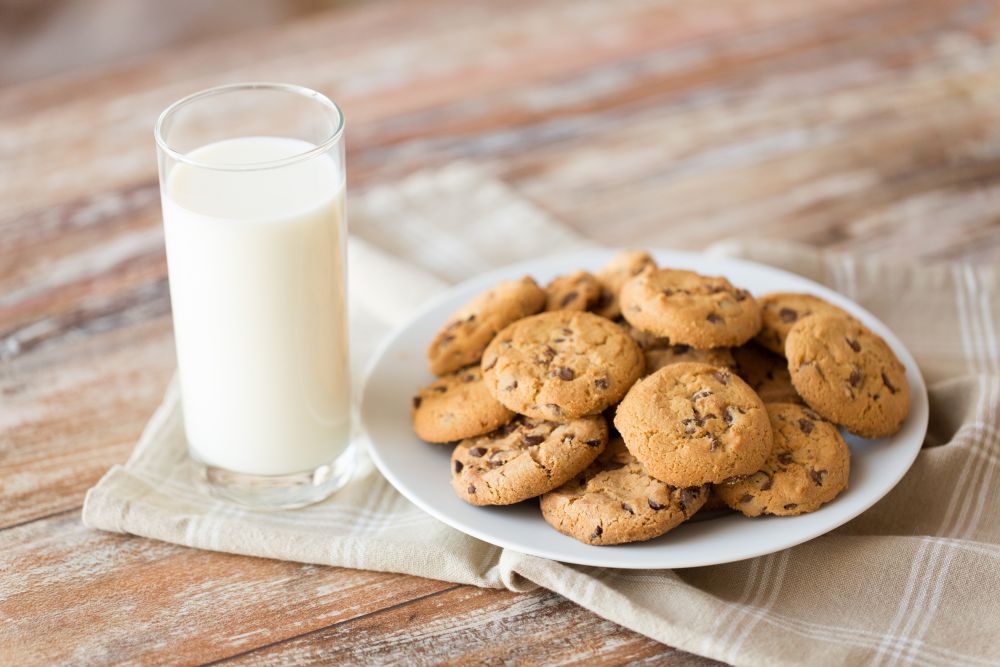 food, junk-food and eating concept - close up of oatmeal cookies with chocolate chips and glass of milk on plate. close up of oatmeal cookies and glass of milk