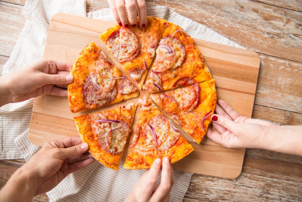 food, people and eating concept - close up of hands sharing sliced homemade pizza on wooden table. close up of hands sharing pizza on wooden table