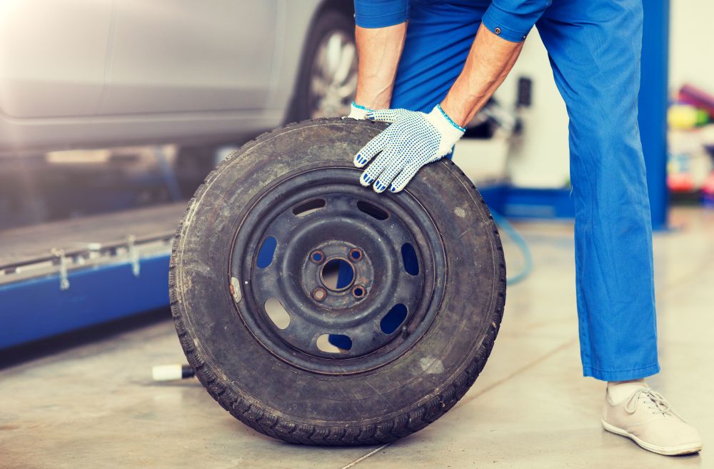 car service, repair, maintenance and people concept - auto mechanic man with wheel tire at workshop. mechanic with wheel tire at car workshop