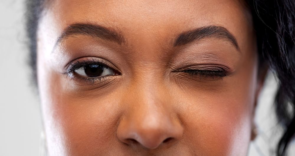 vision, make up and people concept - close up of african american woman face winking one eye. close up of african american woman winking one eye