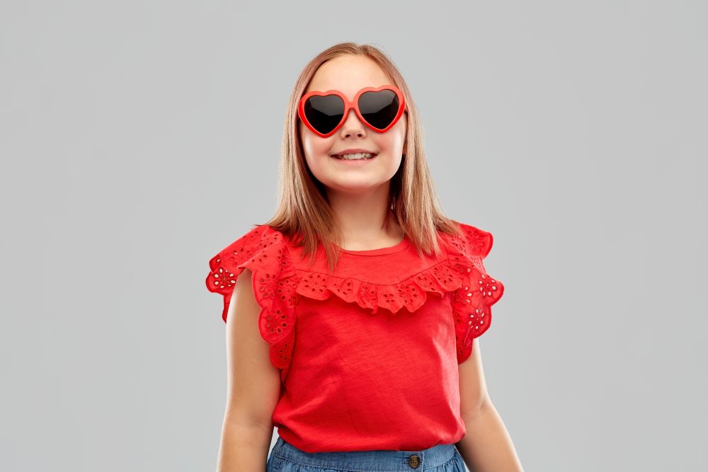 childhood, valentine&rsquo;s day and summer concept - smiling preteen girl with heart shaped sunglasses over grey background. smiling preteen girl with heart shaped sunglasses