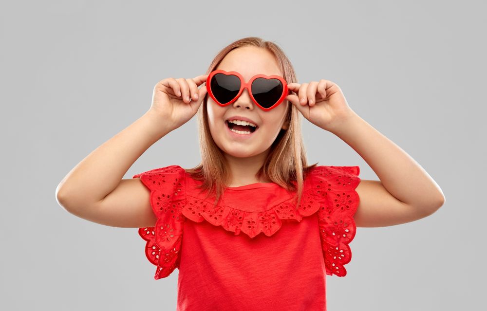 childhood, valentine&rsquo;s day and summer concept - happy preteen girl with heart shaped sunglasses over grey background. happy preteen girl with heart shaped sunglasses