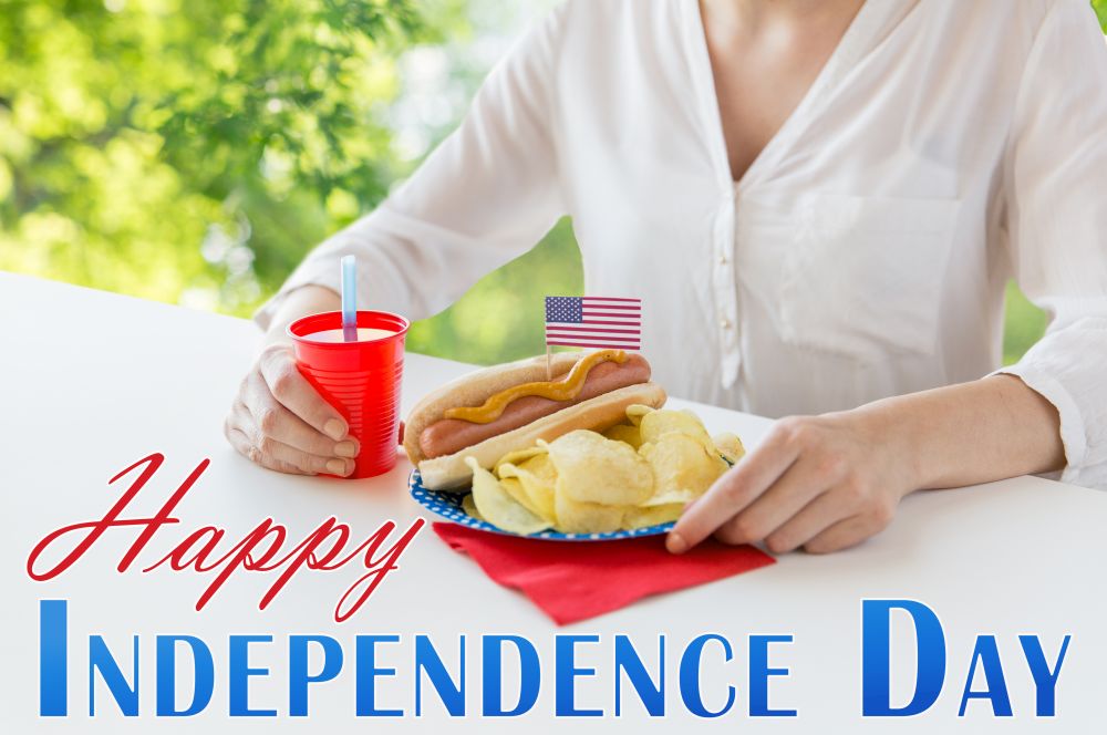 independence day, celebration and holidays concept - close up of woman with hot dog decorated by american flag, potato chips and juice celebrating 4th july over green natural background. woman celebrating american independence day