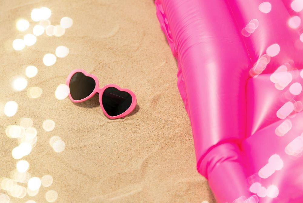 vacation and summer holidays concept - pink sunglasses and swimming mattress on beach sand. sunglasses and pink swimming mattress on beach