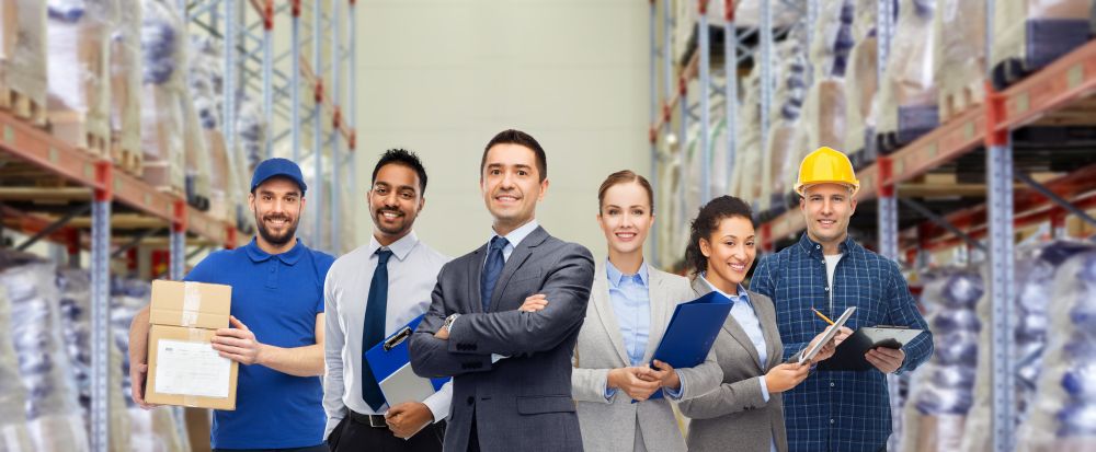 logistic business, delivery service and people concept - happy international team of employees over warehouse background. group of business people and warehouse workers