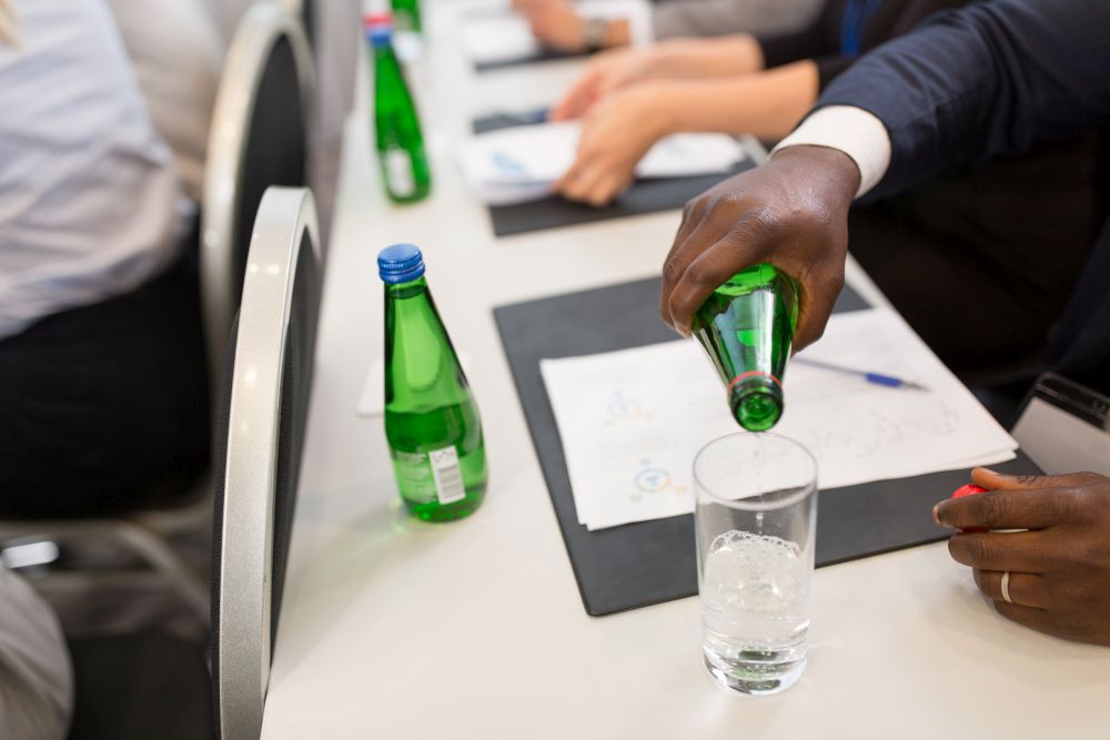 business and people concept - close up of african american businessman pouring water from bottle to glass at conference. businessman pouring water to glass at conference