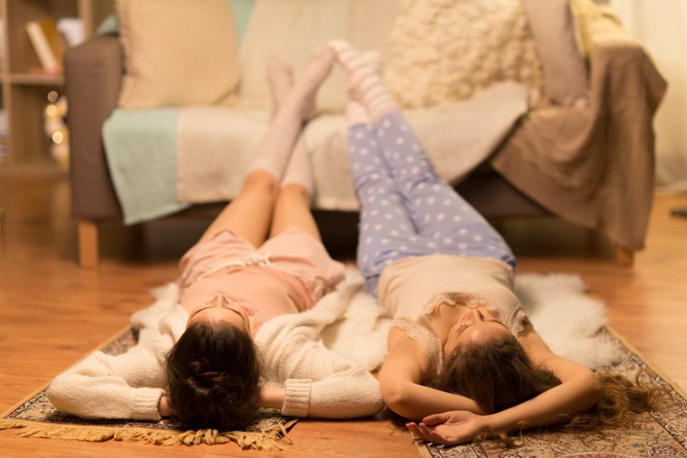 friendship, hygge and pajama party concept - happy female friends or teenage girls lying on floor at home. female friends lying on floor at home pajama party