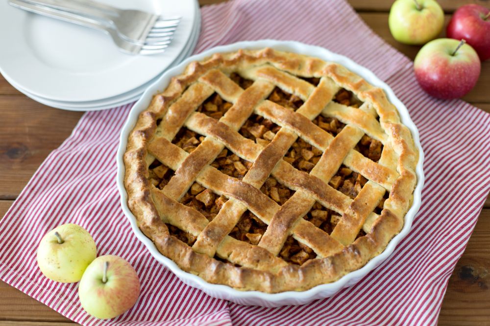food, culinary and baking concept - apple pie and kitchen towel on wooden table. apple pie in baking mold on wooden table