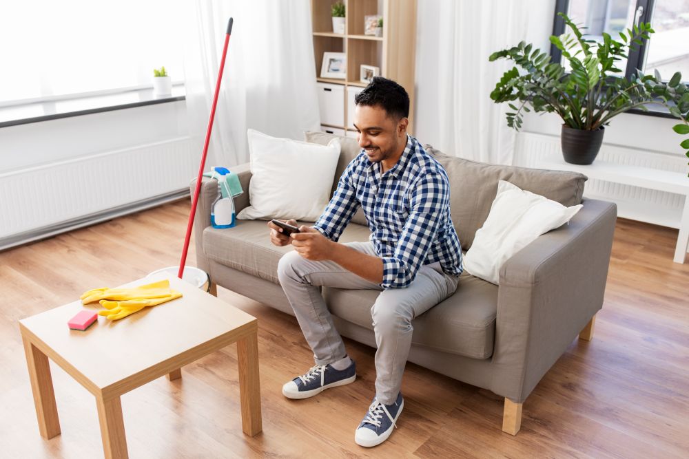 household and technology concept - smiling indian man playing game on smartphone after cleaning home. man playing game on smartphone after cleaning home
