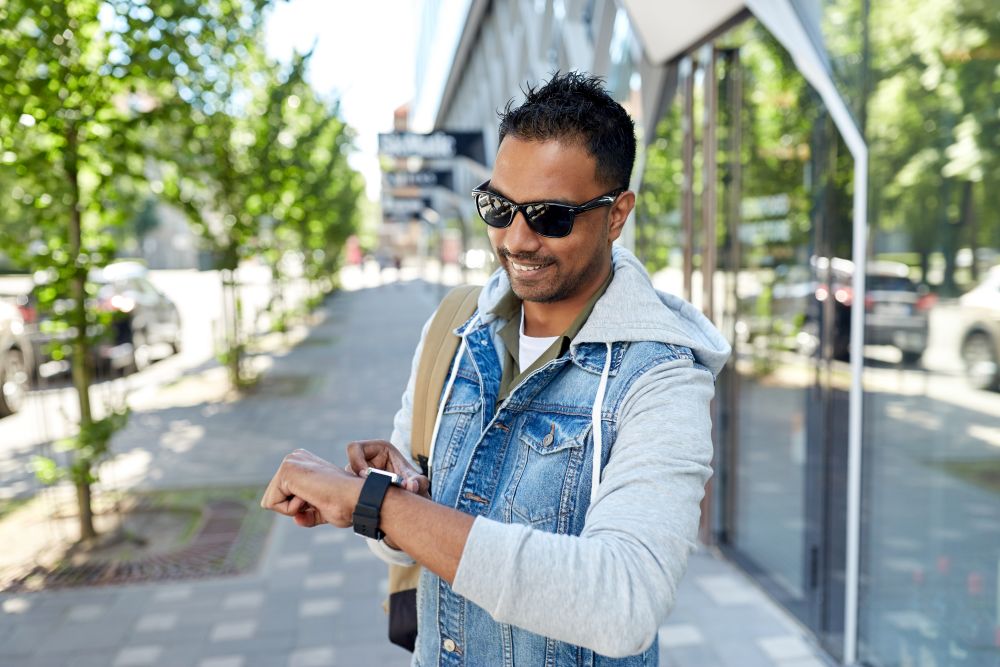 travel, tourism and lifestyle concept - smiling indian man with smart watch and backpack walking along city street. indian man with smart watch and backpack in city