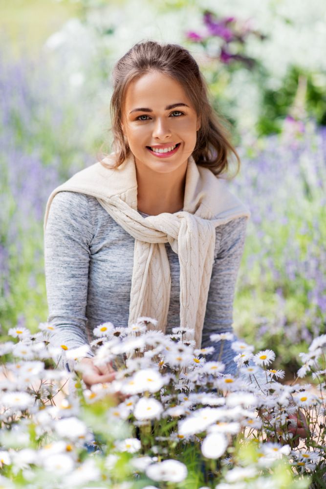 gardening and people concept - happy young woman with chamomile flowers at summer garden. young woman with flowers at summer garden