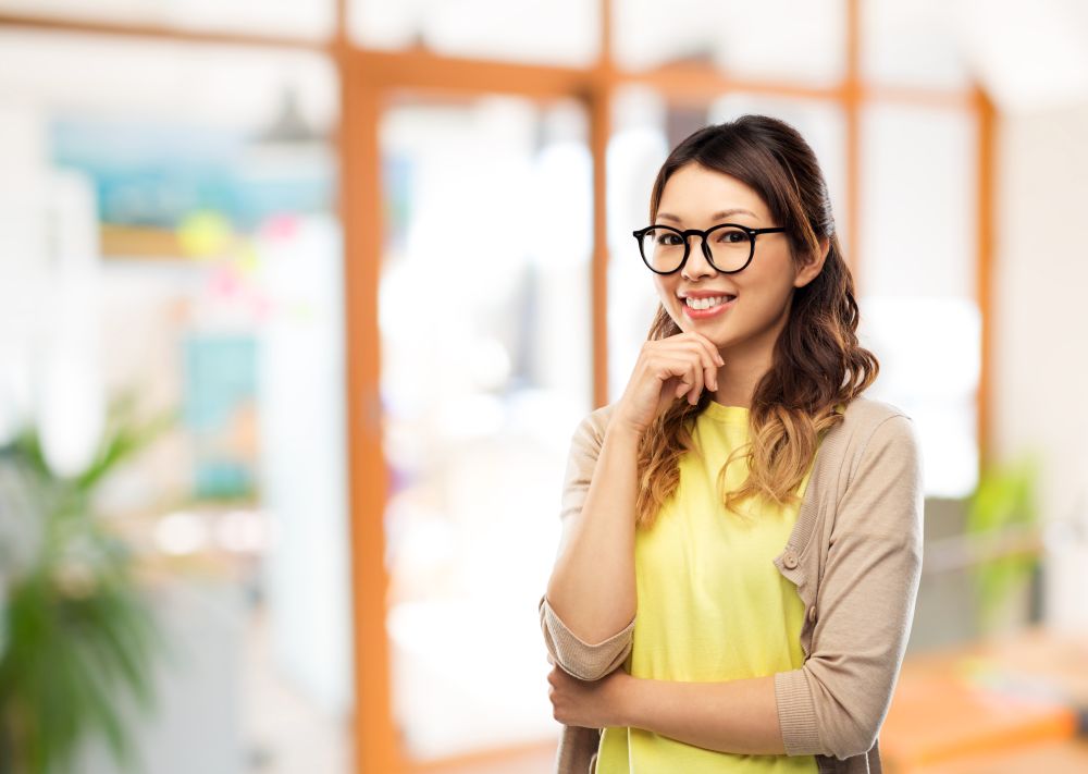 people, education and school concept - happy asian woman in glasses or student over office background. happy asian woman in glasses or student