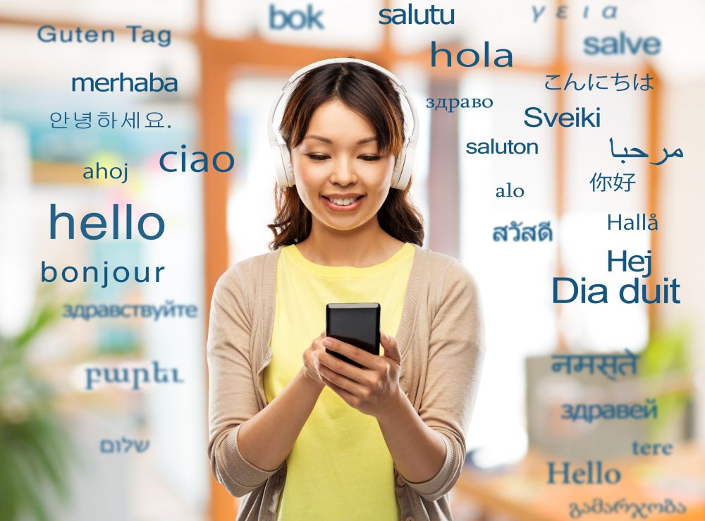 education, communication and technology concept - happy asian young woman in headphones listening to music on smartphone over greeting words in different foreign languages. asian woman in headphones listening to music