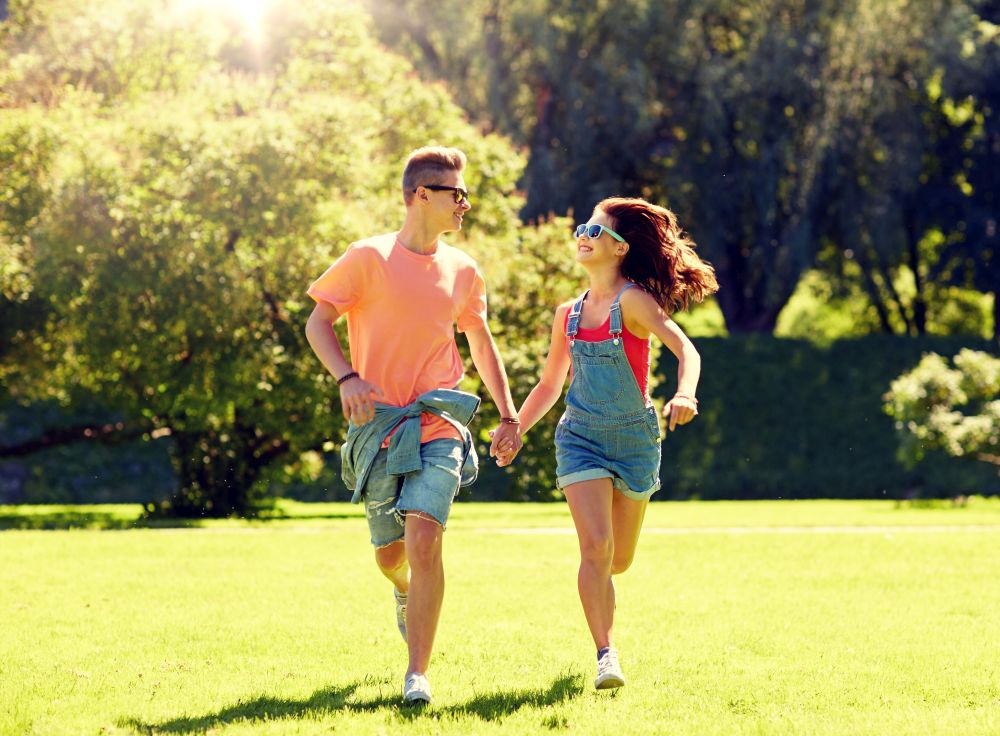 holidays, vacation, love and people concept - happy smiling teenage couple holding hands and running at summer park. happy teenage couple running at summer park
