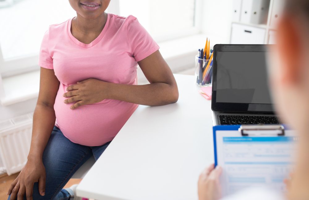 pregnancy, gynecology and medicine concept - gynecologist doctor with clipboard and pregnant african american woman patient meeting at hospital. gynecologist and pregnant woman at hospital