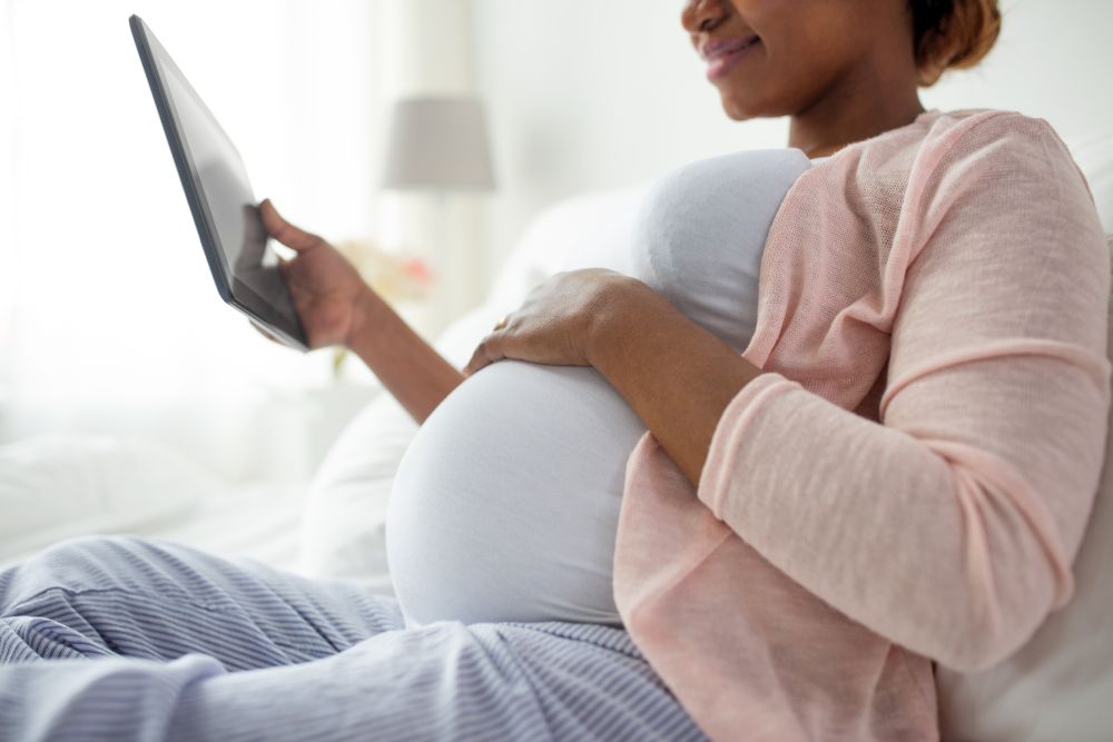 pregnancy, technology and people concept - close up of pregnant african american woman with tablet pc computer in bed at home. close up of pregnant woman with tablet pc at home