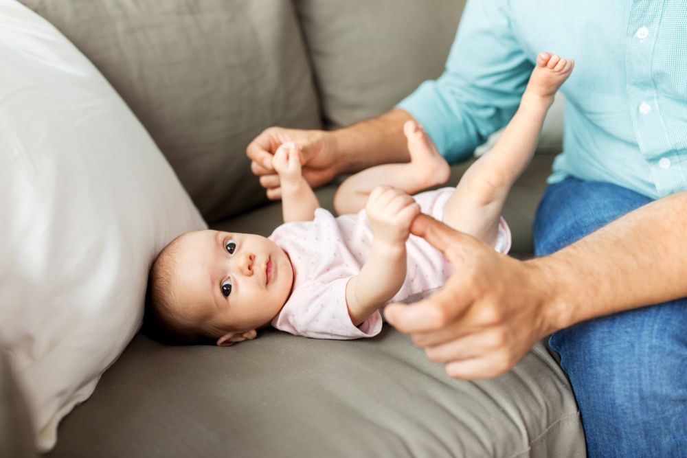 family, parenthood and fatherhood concept - middle aged father playing with little baby daughter lying on sofa at home. middle aged father playing with baby at home