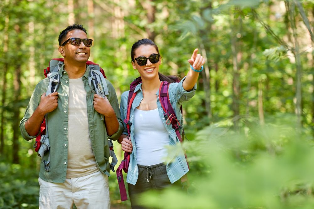 travel, tourism, hike and people concept - mixed race couple with backpacks in forest. mixed race couple with backpacks hiking in forest