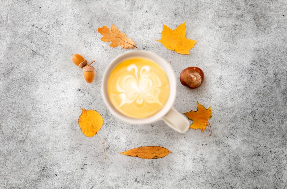 drinks, season and latte art concept - cup of coffee with butterfly on foam, autumn leaves, acorns and chestnut on grey stone background. cup of coffee, autumn leaves, acorns and chestnut
