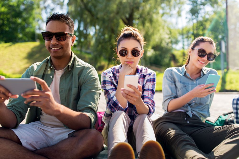 friendship, technology and travel concept - group of friends with smartphones at summer park. friends with smartphones at summer park