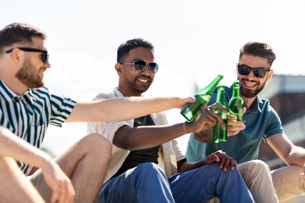 leisure, male friendship and people concept - happy men or friends toasting and drinking beer on street in summer. happy male friends drinking beer on street