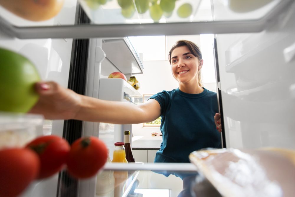 healthy eating, food and diet concept - happy woman taking apple from fridge at home kitchen. happy woman taking food from fridge at home