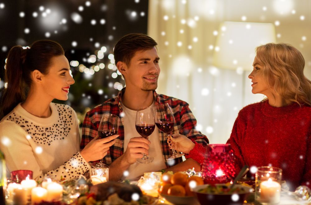 holidays and celebration concept - happy friends having christmas dinner at home, drinking red wine and clinking glasses over snow. happy friends drinking red wine at christmas party