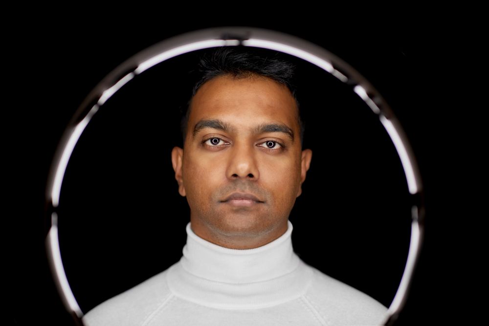 future technology concept - indian man over white illumination on black background. man in glasses over white illumination on black