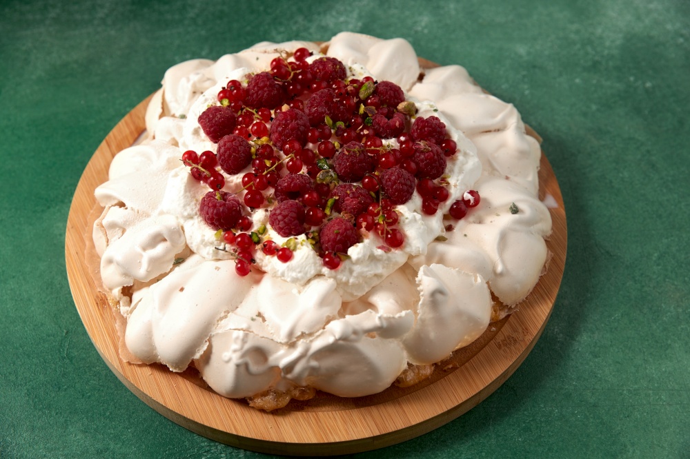 food, culinary, baking and cooking concept - close up of pavlova meringue cake decorated with red berries on wooden serving board. pavlova meringue cake with berries on wooden board