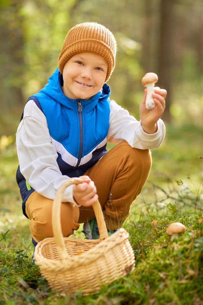 picking season, childhood and people concept - happy smiling little boy with basket picking mushrooms in forest. happy boy with basket picking mushrooms in forest
