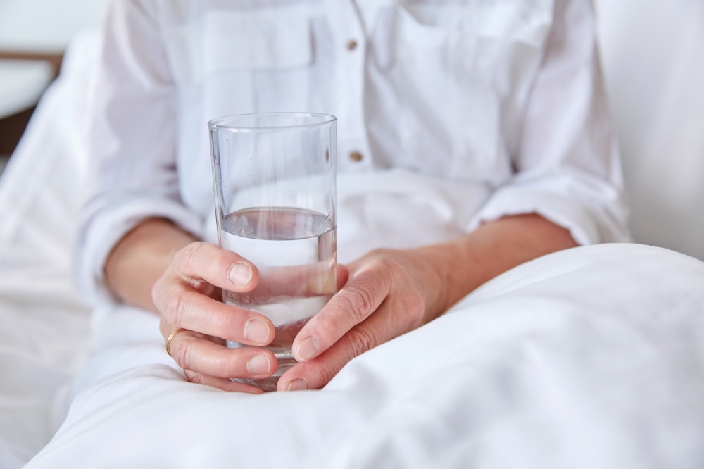medicine, healthcare and people concept - close up of senior woman with glass of water sitting in bed at hospital ward. close up of senior woman with water at hospital