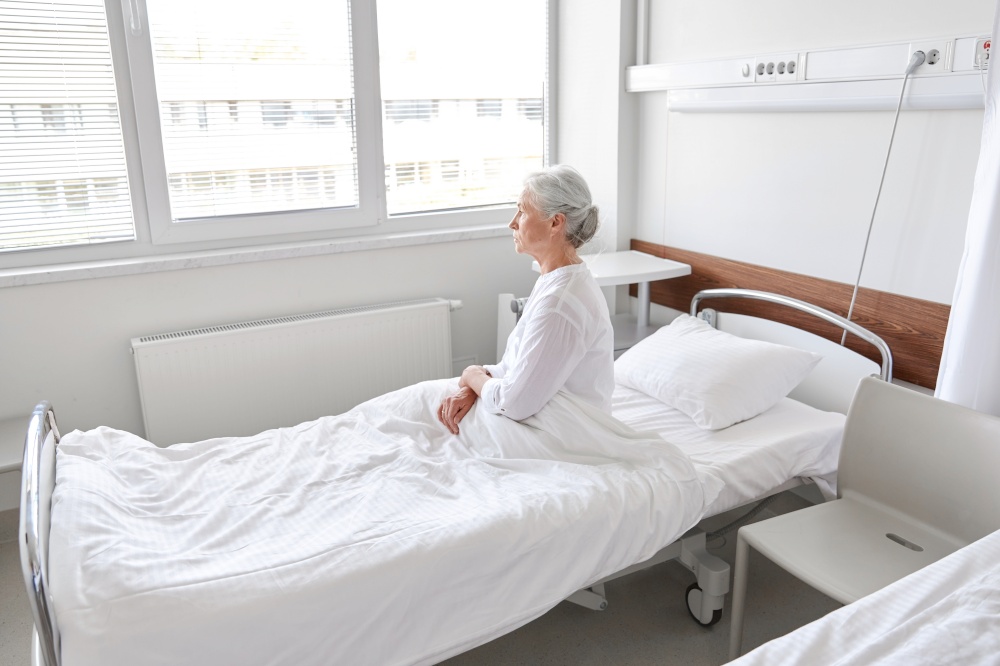 medicine, healthcare and people concept - lonely senior woman sitting in bed at hospital ward. lonely senior woman sitting in bed at hospital