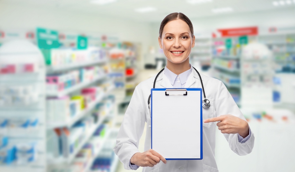 medicine, profession and healthcare concept - happy smiling female doctor in white coat showing clipboard over pharmacy background. happy female doctor with clipboard at pharmacy