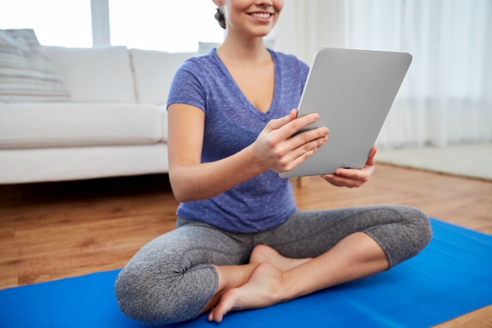 fitness, technology and healthy lifestyle concept - happy smiling woman with tablet pc computer doing yoga at home. woman with tablet pc computer doing yoga at home