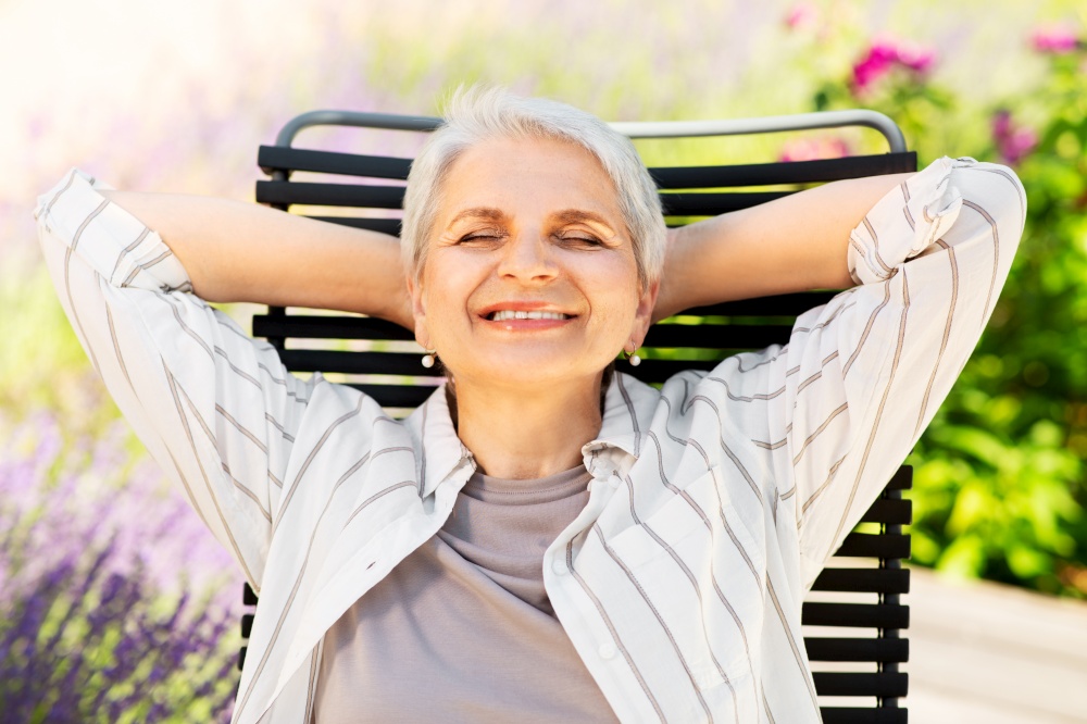 old age, retirement and people concept - happy smiling senior woman resting on chair at summer garden. happy senior woman resting at summer garden
