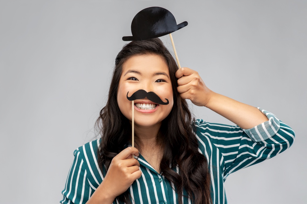 party props, photo booth and people concept - happy asian young woman with big black moustaches and bowler hat over grey background. asian woman with vintage moustaches and bowler hat