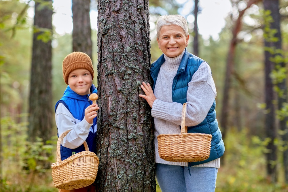 season, leisure and people concept - happy smiling grandmother and grandson with baskets picking mushrooms in forest. grandmother and grandson with mushrooms in forest