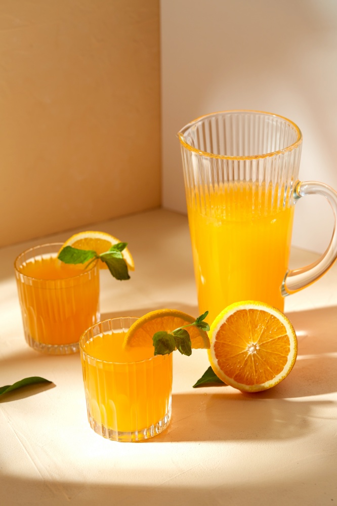 drink, detox and diet concept - glasses with fruit orange juice and peppermint on table. glasses with orange juice and peppermint on table