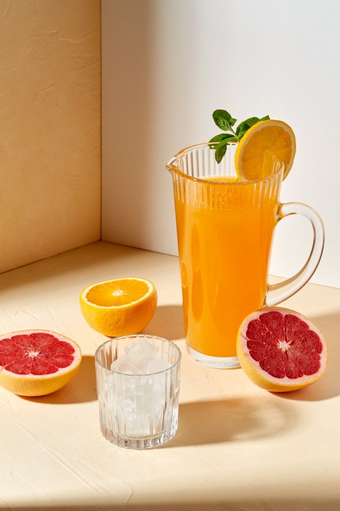 drink, detox and diet concept - jug with orange juice, cut grapefruit and ice cubes in glass on table. orange juice, grapefruit and ice in glass on table