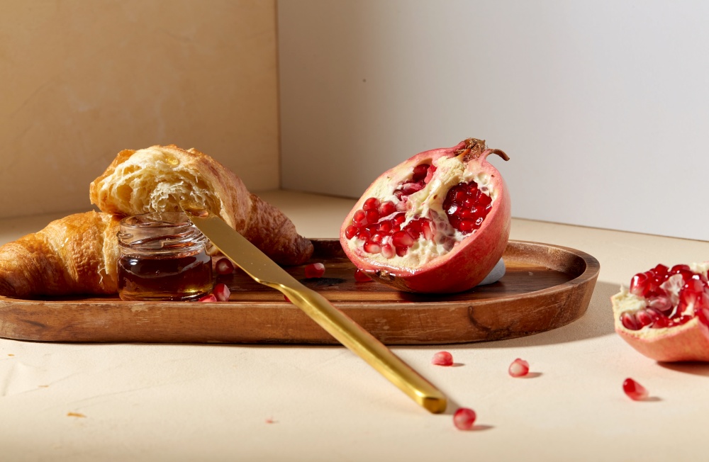 food and eating concept - croissant, pomegranate and honey with table knife on wooden tray. croissant, pomegranate and honey on wooden tray