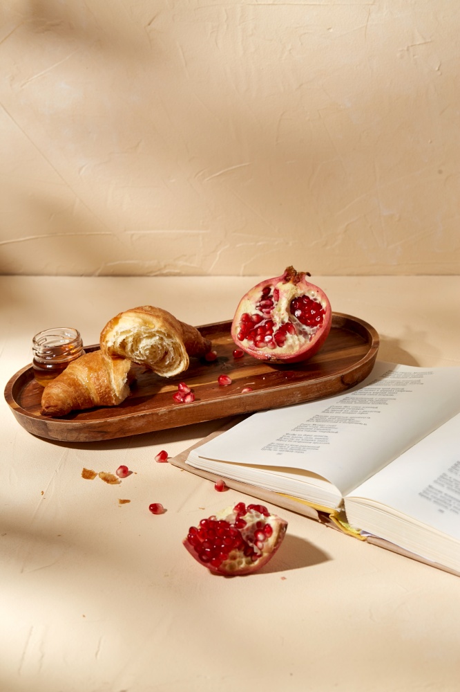food and eating concept - open book, croissant, pomegranate and honey on wooden tray. book, croissant, pomegranate and honey on tray