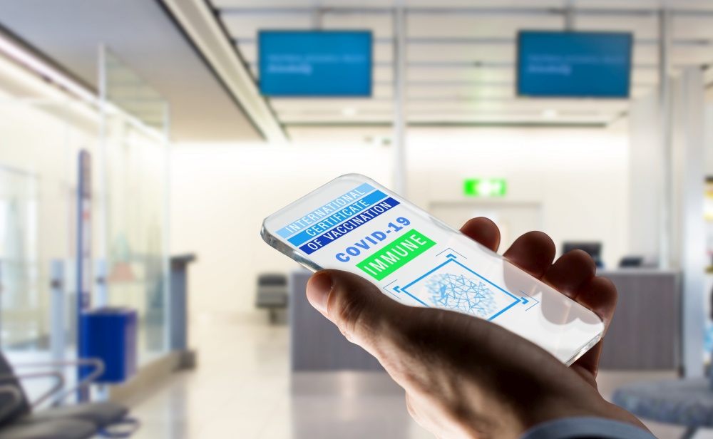 safe travel, technology and health care concept - close up of hand holding smartphone with international certificate of vaccination or virtual immunity passport on screen over airport background. hand holding phone with certificate of vaccination