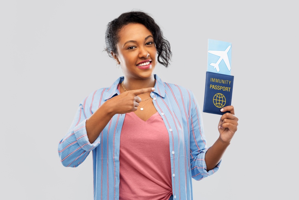 safe travel, tourism and health care concept - happy young african american woman with air ticket and passport over grey background. happy woman with air ticket and immunity passport