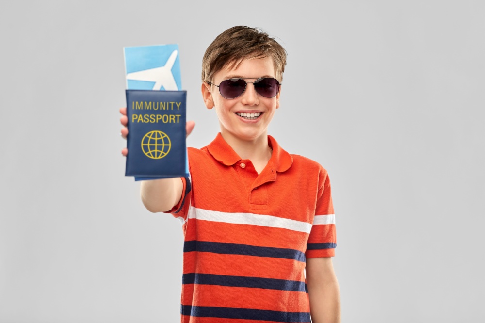 safe travel, tourism and health care concept - portrait of happy smiling boy in sunglasses and red polo t-shirt with air ticket and immunity passport over grey background. happy boy with air ticket and immunity passport