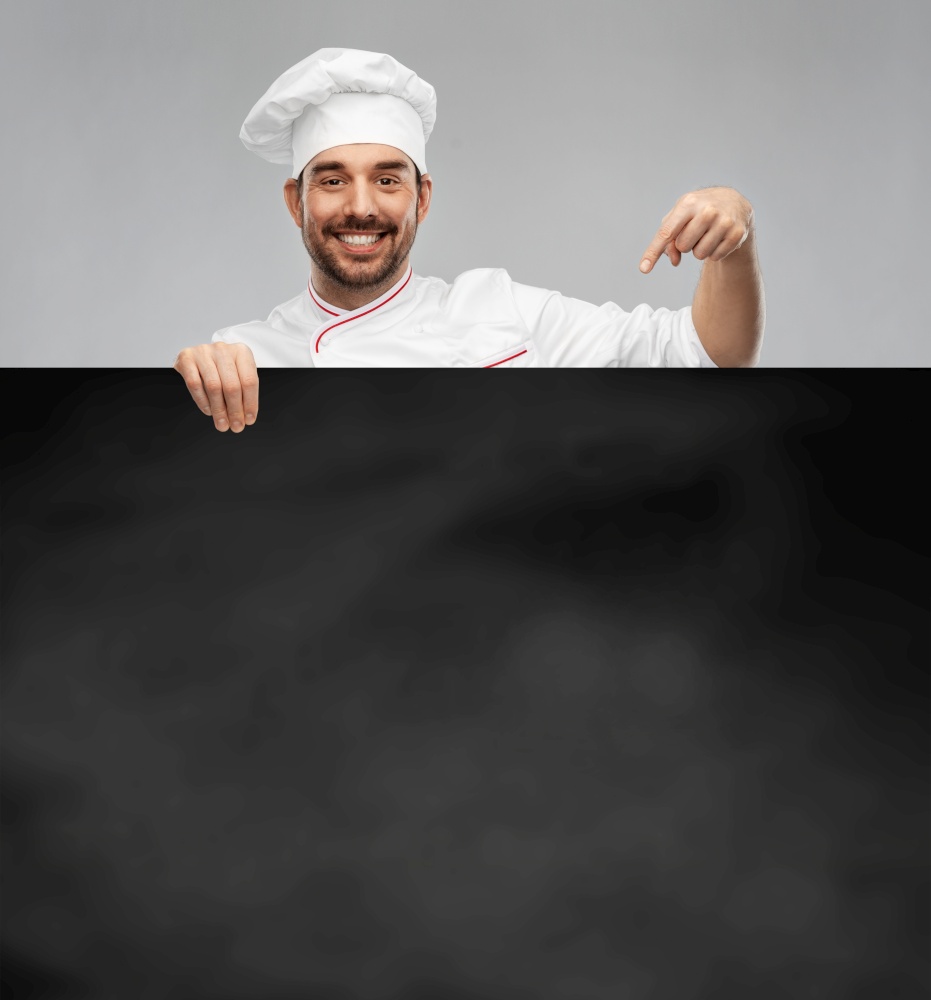 cooking, culinary and people concept - happy smiling male chef in toque with big black chalkboard over grey background. happy smiling male chef with big black chalkboard
